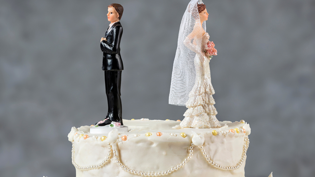 Das Bild zeigt eine Hochzeitstorte mit zwei Brautfiguren darauf, die sich voneinander wegdrehen.