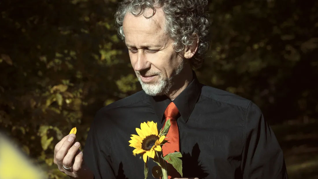Mann mit Sonnenblume, in einer Hand hält er ein Blütenblatt
