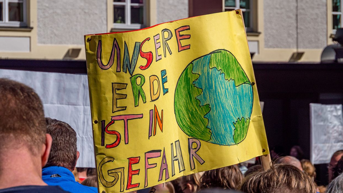 Es wird ein Transparent mit der Aufschrift "Unsere Erde ist in Gefahr" auf einer Klimademo gezeigt.